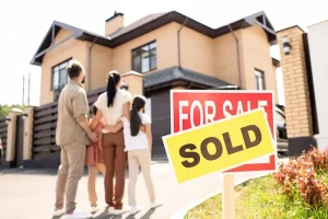 Family standing in front of a house with a "Sold" sign.